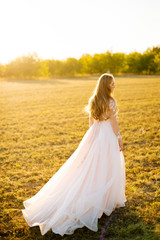 Fototapeta na wymiar Silhouette of a young woman in her bridal dress at sunset in field.