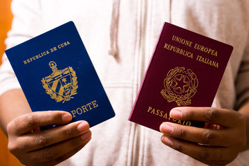 Young black person holding two passports in hands. Official passport of Cuba, official passport of Italy