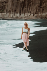 Fototapeta premium blond woman on a black beach on Santorini, with cliff in the background and a rough sea
