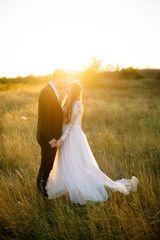 Young happy couple is kissing in the field at sunset.