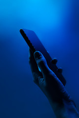 Hand holds smartphone. Neon classic blue light, vertical photo. Copyspace. Technology concept, future, social networks, content, mobile.