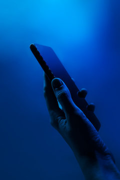 Hand holds smartphone. Neon classic blue light, vertical photo. Copyspace. Technology concept, future, social networks, content, mobile.