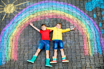 two school kids boys having fun with with rainbow picture drawing with colorful chalks on asphalt....