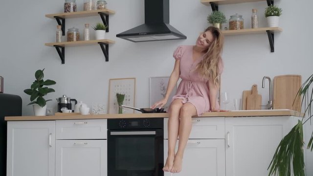 happy girl sitting on the kitchen table and carefree dangles legs