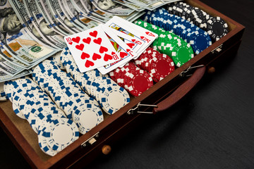 Colorful poker chips with playing cards and american dollars on dark background.