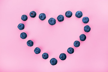 Blueberry berries heart-shaped lying on a pink background.