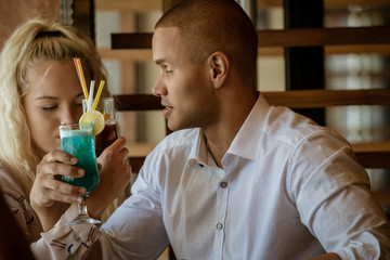 Young african man and blonde american woman drink cocktail, happy couple in bar drink cocktail and have fun