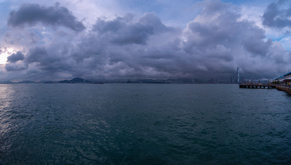 Obraz premium a merged panorama of victoria harbour and the upcoming storm above in hong kong, china