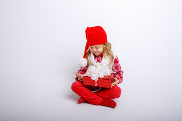 cute happy little girl in santa claus hat. Santa's assistant is smiling and sitting with gifts on a white background