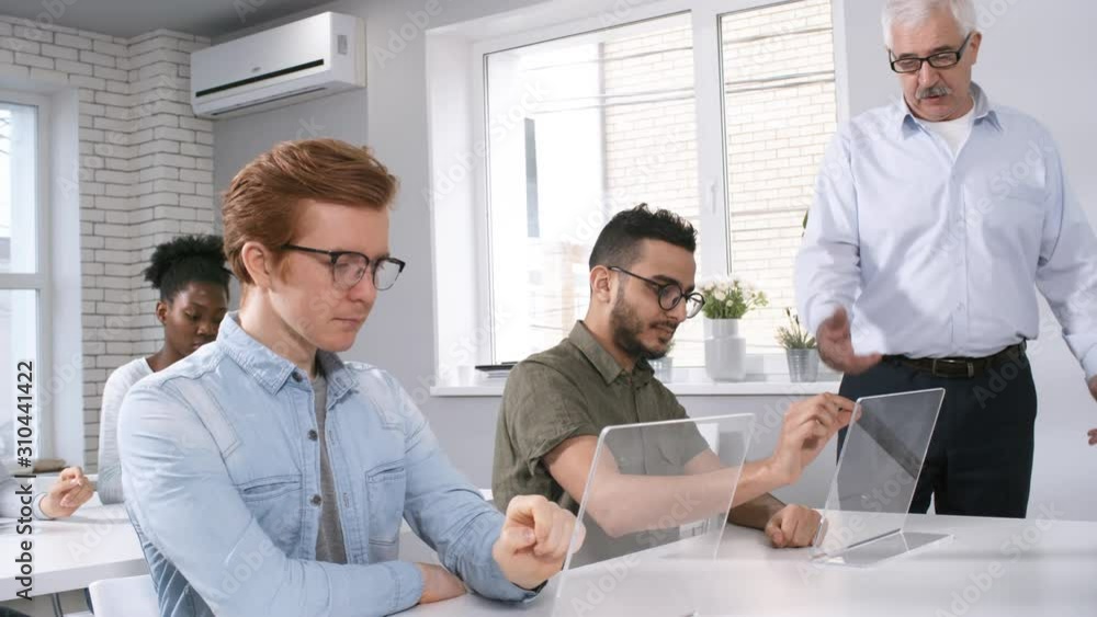 Poster medium tracking shot of senior male caucasian professor walking around classroom and checking on stu