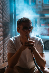 Silhouette of hookah maker blowing smoke in the dark.