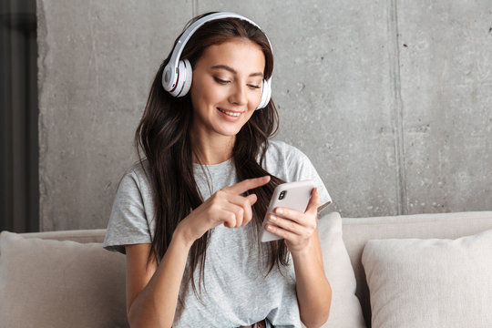 Image of woman in headphones holding smartphone while sitting on sofa