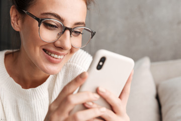 Image of woman in eyeglasses smiling and holding cellphone at home