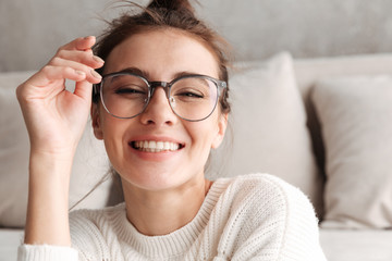 Image of young woman in eyeglasses smiling while resting on sofa at home
