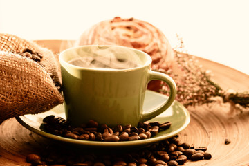 Cup of coffee with sweet bun with raisins and coffee beans on a wooden table with vintage deko
