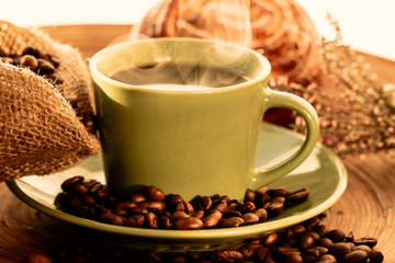 Cup of coffee with sweet bun with raisins and coffee beans on a wooden table with vintage deko