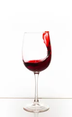 Fotobehang A glass of red wine with a splash on the table on a white background. Vertical photo © Александра Туркина