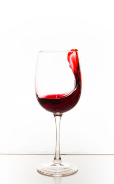 A glass of red wine with a splash on the table on a white background. Vertical photo