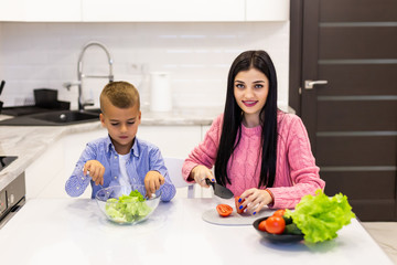 Young mother with son boy cooking salad mom sliced vegetables food son tasting salad. Happy family cook food enjoyment lifestyle kitchen
