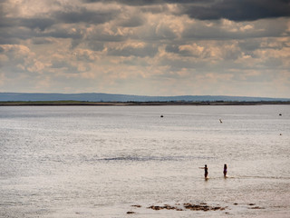 Fototapeta na wymiar Silhouette of two women walking in water for a swim. cloudy sky over ocean, Mountains in the background. Galway bay.
