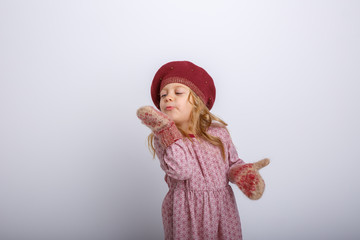 portrait of a small smiling girl in gloves and hat blows snow off her hands on a gray background