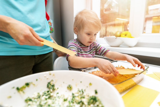 Mother Cooking Together With Child In Home Kitchen. Putting Lasagne Sheets