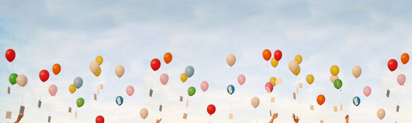 Panoramic background, colorful flying balloons. hands holding colored balloons with greeting cards. Bunch of flying balloons on blue sky background. Concept of happiness and joy, for banner, poster