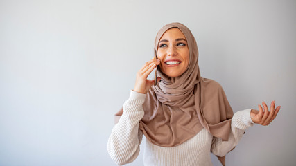 Portrait of young arab woman 20s in islamic headscarf with oriental makeup talking with cell phone isolated over gray background. Portrait of happy muslim woman using mobile phone