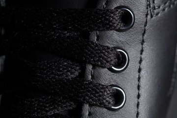 Part of a black boot with laces. A fragment of dark shoes. A piece of sneaker.