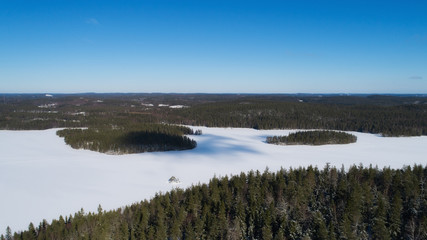 Aerial view of a white snowy lake in winter, clouds on a blue sky create shadows on the surface at sunny day. Beautiful landscape of northern nature with drone.
