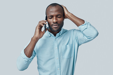 Frustrated young African man talking on the smart phone while standing against grey background