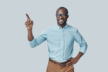 Charming young African man pointing copy space and smiling while standing against grey background