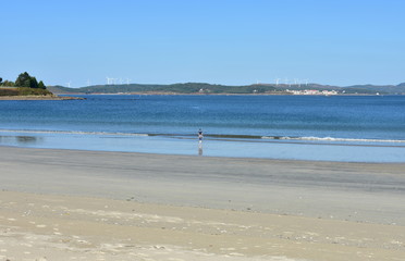 Fototapeta na wymiar Beach with wet sand, woman and blue sky. Muxia, Spain.