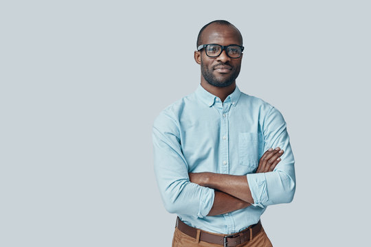 Confident young African man looking at camera and smiling while standing against grey background