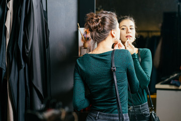 Woman shopping choosing dresses looking in mirror uncertain. Beautiful young multicultural shopper in clothing store.