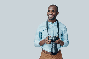 Handsome young African man looking away and smiling while standing against grey background