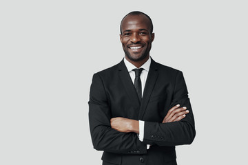 Handsome young African man in formalwear looking at camera and smiling while standing against grey background