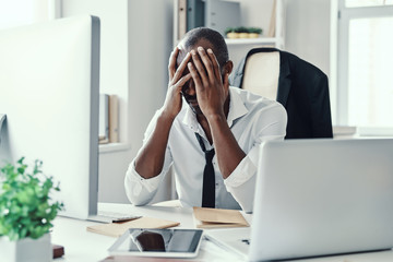 Frustrated young African man in formalwear keeping head in hands head while working in the office