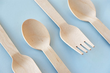 Eco cutlery from pine wood. Disposable tableware from natural materials. Wooden spoon and fork agains a pastel blue background. Image with copy space. Zero waste, plastic free, stop pollution concept.