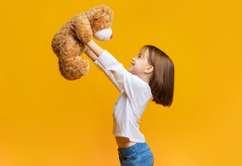 Happy girl playing with teddy bear over yellow background