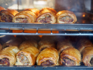 Closeup detail of multiple freshly-baked sausage rolls, a traditional British pastry, sold on racks at a street vendor. London, United Kingdom. Travel and food. - 310449616