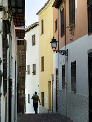 Fototapeta na wymiar Rear view of a man walking narrow alley of old buildings in town, Granada, Granada Province, Spain
