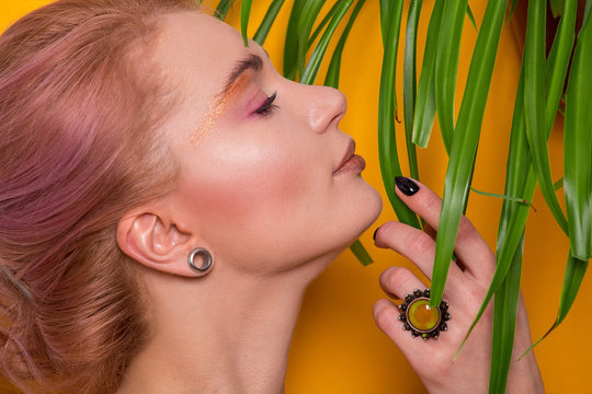 Shiny golden make-up on a beautiful young European girl model and leaves of a green plant isolated on an orange background in a photo studio