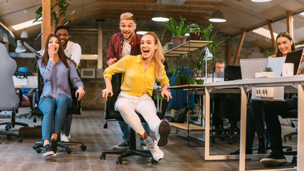 Office fun. Joyful coworkers enjoying office chair race