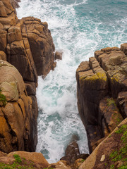 Wide aerial view of waves crashing in between the prismatic granite cliffs of Porthcurno beach. Vertical orientation. Cornwall, United Kingdom. Travel and nature. - 310450280