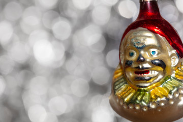 Vintage decorative christmas bauble in a shape of a crown jester against a silver bokeh blury star background.