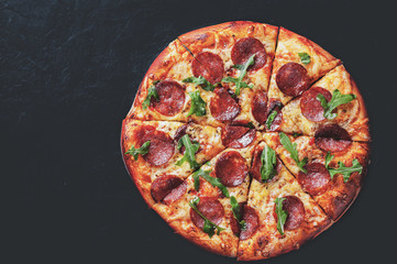 Pepperoni Pizza with Mozzarella cheese, salami, Tomato sauce, pepper, Spices and Fresh arugula. Italian pizza on Dark grey black slate background