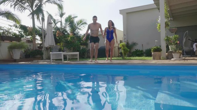 Young couple jump into pool celebrating success
