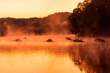 Silhouette of the rafting boat in the golden misty lake under the warm morning sunlight in Pang Ung