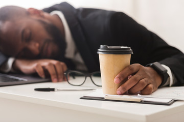 Exhausted business clerk holding cup of coffee, sleeping at workplace